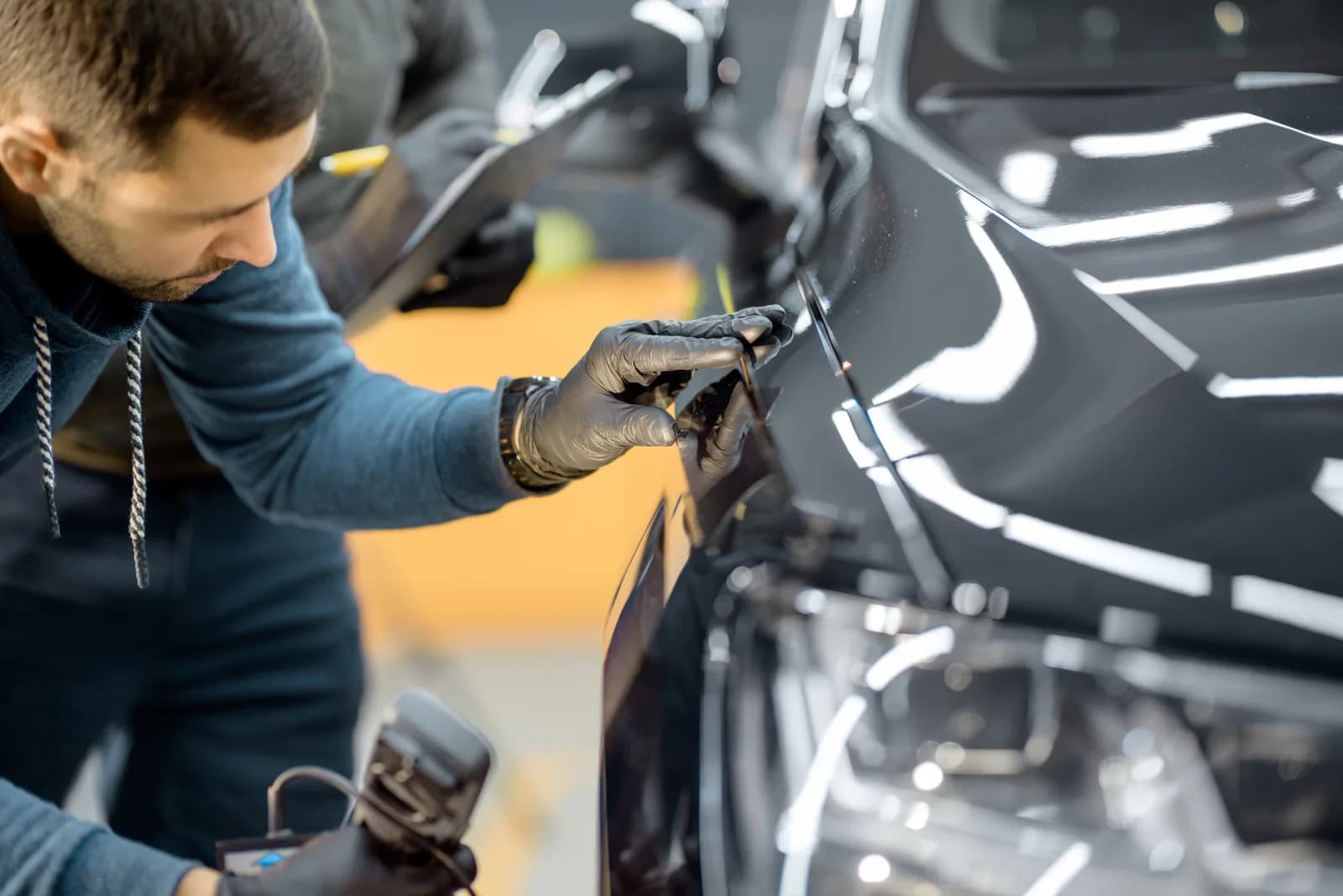 Skilled technician performing precision paintless dent repair on a glossy black vehicle